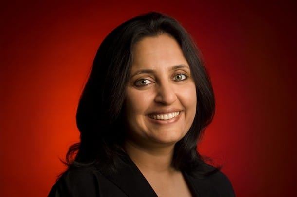 Headshot of Sonal Shah wearing a black suit on a red background.